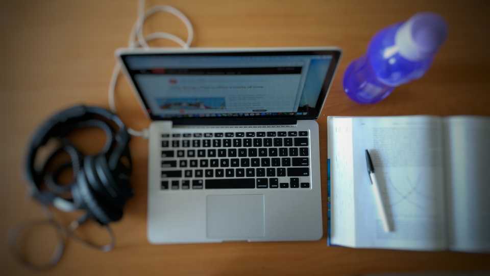 Desk showing headphones, a laptop, a book and a pen